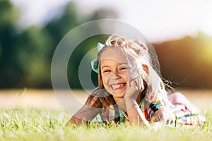 Little smiling girl laying on the grass field in the park.