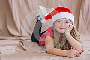 Little smiling girl in a red t-shirt with a santa claus hat lies on her stomach and smiles