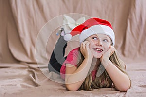 Little smiling girl in a red t-shirt with a santa claus hat lies on her stomach and smiles