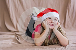 Little smiling girl in a red t-shirt with a santa claus hat lies on her stomach and smiles