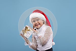 Waist up portrait of a little smiling blonde girl  with Sante Claus`s cap holding a gift box photo