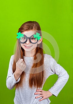 Little smiling girl in shamrock clover glasses for irish St. Patrick's Day on green background