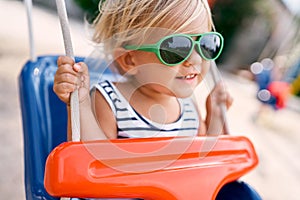 Little smiling girl in sunglasses on a swing
