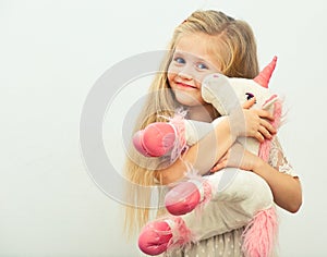 Little smiling girl with white unicorn toy.