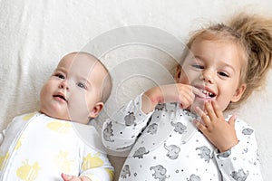 Little smiling kids playing together sitting on bed. Brother and sister show a newborn a toy. kids meeting new born