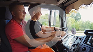 Little smiling red-haired child holds his hands on steering wheel sitting on lap of daddy and learning to drive the