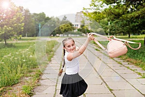 A little smiling school girl with pigtails throwing her bagpack in school yard photo