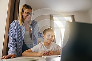 Smiling mom helping her son doing homework studying online using laptop in home