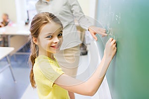 Little smiling schoolgirl writing on chalk board