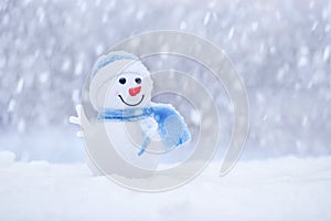 Little snowman in a cap and a scarf on snow in the winter. Happy snowman with snowball. Christmas card, copy space
