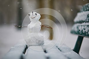 Little snowman with happy face on a bench covered with snow