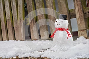 Little snowman stands in front of a wooden fence