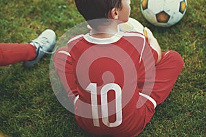 Little soccer forward player boy sitting on grass