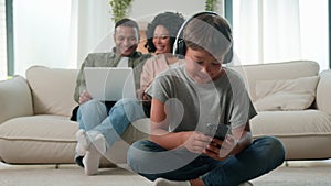 Little son boy child in headphones play video game on mobile phone happy multiracial mom dad and preschool kid using