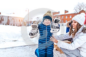 Little son, cheerful joyful boy of 4-6 years old, holds his skates his hands. Mom woman supports him. Caring a change of