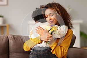Young mixed race woman mother with flower bouquet embracing son while getting congratulations on Mother`s day