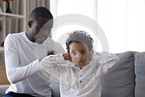 Little son covering ears, ignoring strict angry African American father
