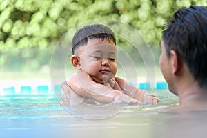 Little son enjoys playing in the pool with Father
