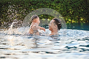 Little son enjoys playing in the pool with Father