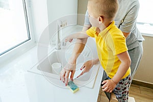 The little son helps his mother with household chores. Mom and the child wash the dishes.