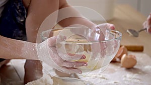 The little son helps mother to involve ingredients on dough in a transparent bowl in kitchen