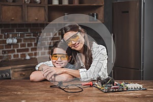 Little son and his beautiful mother hugging while sitting at table with computer motherboard