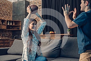 Little son and his beautiful mother playing with a rugby ball while sitting on couch