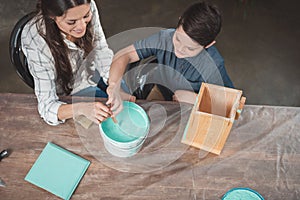 Little son and his beautiful mother sitting at table and painting a