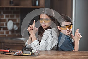 Little son and his beautiful mother wearing protective glasses posing and making gesture as if holding