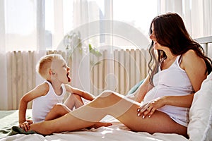 a little son and his pregnant mother are lying on the bed