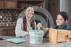 Little son and his young mother painting a wooden birdhouse