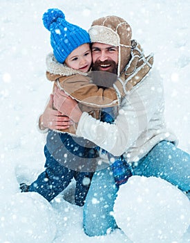 Little son hugs his dad on winter holiday. Daddy and boy smiling and hugging. Father and son play in winter clothes