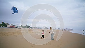 Little son playing kite with parent on beach. Joyful mother helping teach child