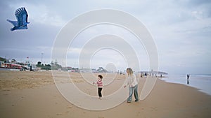 Little son playing kite with parent on beach. Joyful mother helping teach child