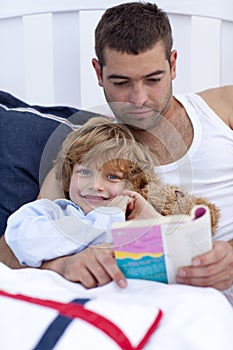 Little son reading with his father in bed