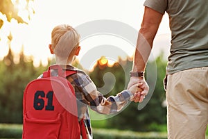 Little son schoolboy with backpack holding hand of father dad while going to first grade in school