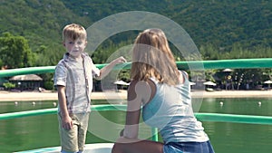 Little son talking with mother aboard sailing ship in summer cruise on sea. Young mom together son traveling on ship