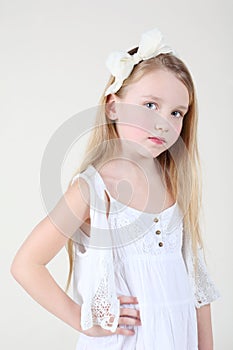 Little sorrowful girl in clean white dress with bow in her hair