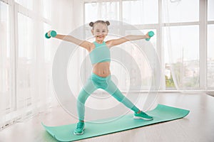 Little sporty girl gymnast in sportswear doing exercises on a mat indoor