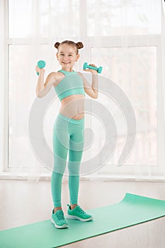 Little sporty girl gymnast in sportswear doing exercises on a mat indoor