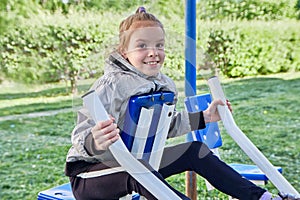 A little sporty girl in a sports uniform is engaged in the exercise machines on the playground for fitness on the street