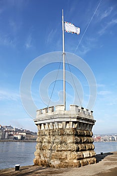 Little stone tower with flag marking the Lipotvaros harbor. The Danube river and a part of the right bank of Budapest