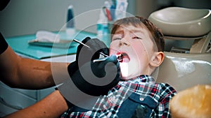 A little stressful boy with damaged baby teeth having a treatment in modern dentistry - examination of the oral cavity