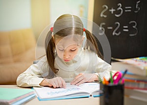 Little student. Beautiful young girl is teaching at home on blackboard. Preschool home education.