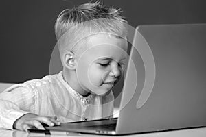 Little student boy using laptop computer in school class. Funny blonde pupil on blackboard.