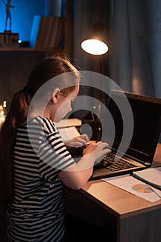 little student girl with laptop computer at home at night. happy student typing on keyboard looking at pc screen