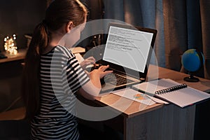 little student girl with laptop computer at home at night. happy student typing on keyboard looking at pc screen