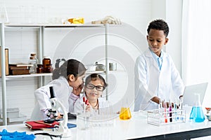Little student group in white lab coat with many laboratory tools on shelves and table in chemistry classroom. A little girl