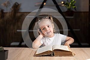 little student preschool elementary school schooled at home and talking on the phone while sitting at a desk. Pupil photo