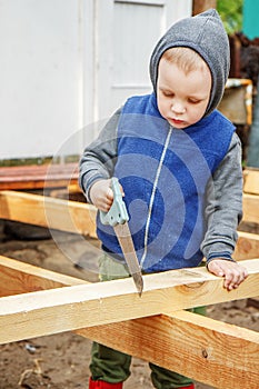 Little studious boy sawing a wooden board. Home construction. Li